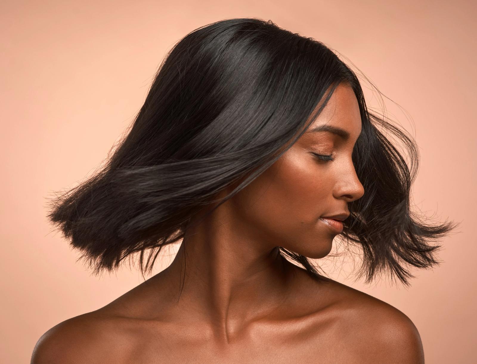 woman with short black hair shaking her hair to the left against a plain pink background