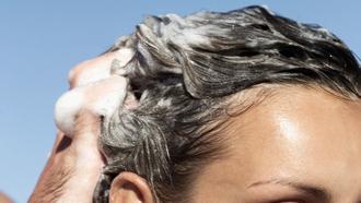 Man massaging shampoo into woman's dark hair outside.