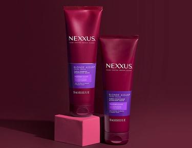 Nexxus Blonde Color Assure Collection, including Shampoo and Conditioner, stands again a dark red background.