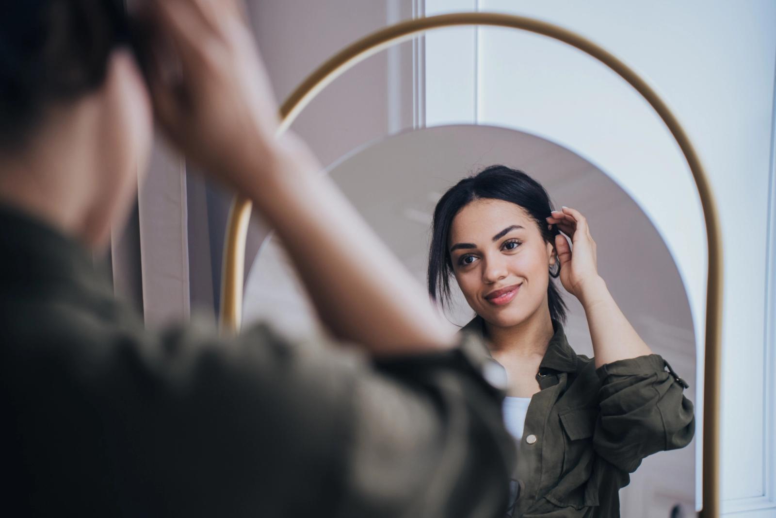 Young woman smiling looking at the mirror, satisfied by her hair.