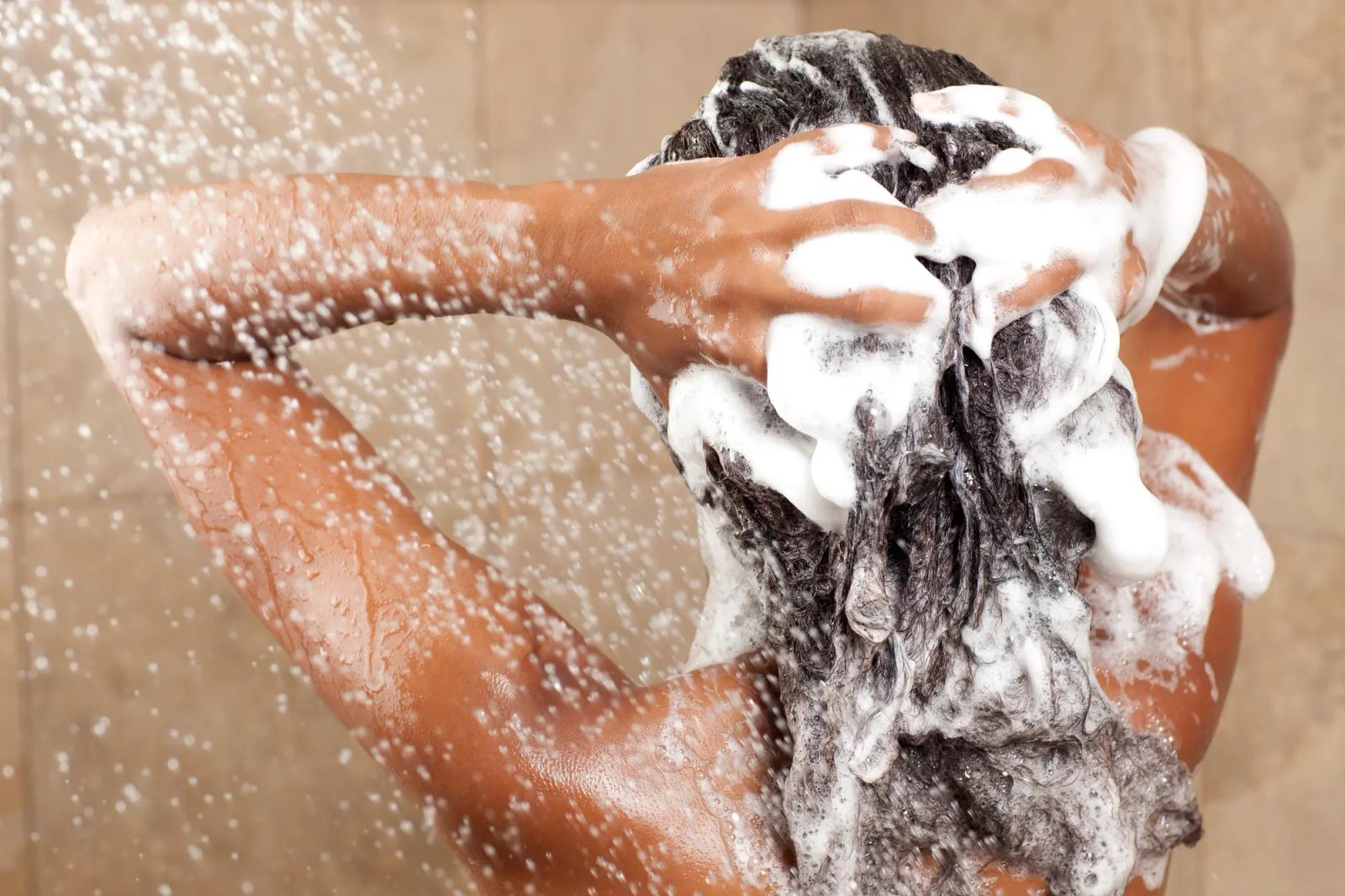 Woman in shower facing the water cascading on her while running her hand trough her wet dark brown hair.