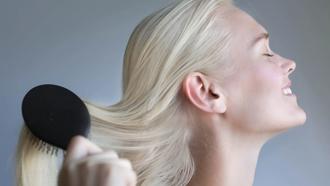 Woman with straight platinum hair smiling to the side while pushing her hair.