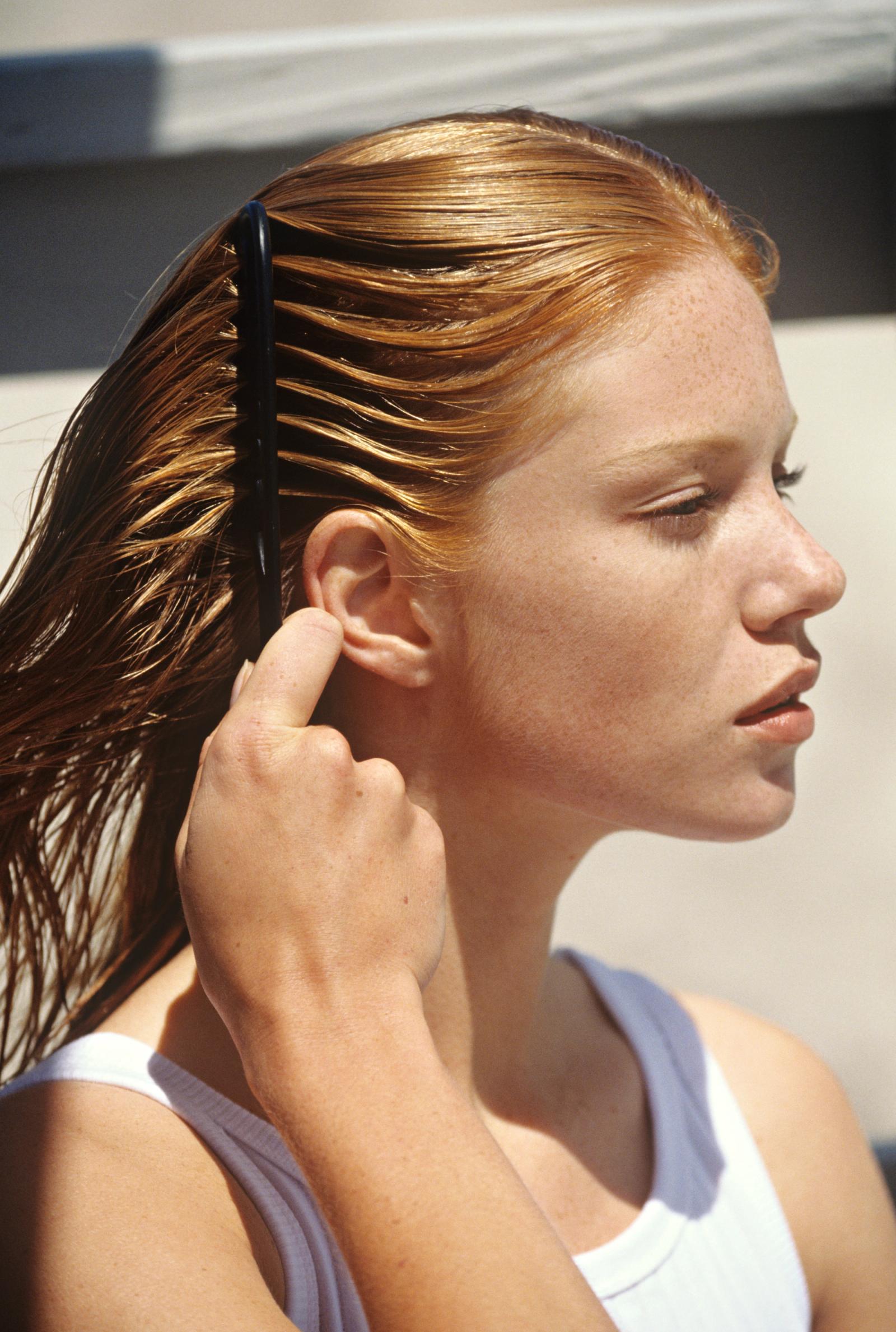 Woman combing product in her hair, whilst sitting in the sun and looking forward