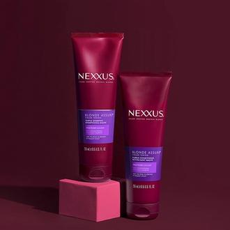 Nexxus Blonde Color Assure Collection bottles lie in diagonal rows on a dark pink background. 