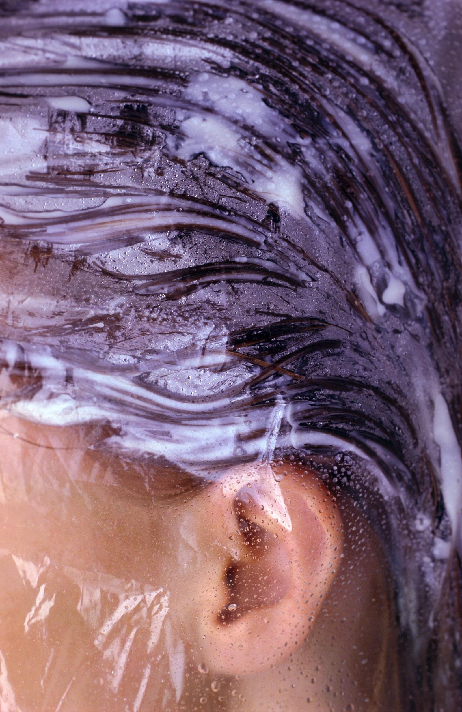 Close up of a woman's hair with shampoo pressed against the shower glass.