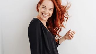 Woman with red hair flipping hair to one side and smiling while standing to the side