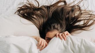Woman with long healthy hair covered in sheet lying in bed