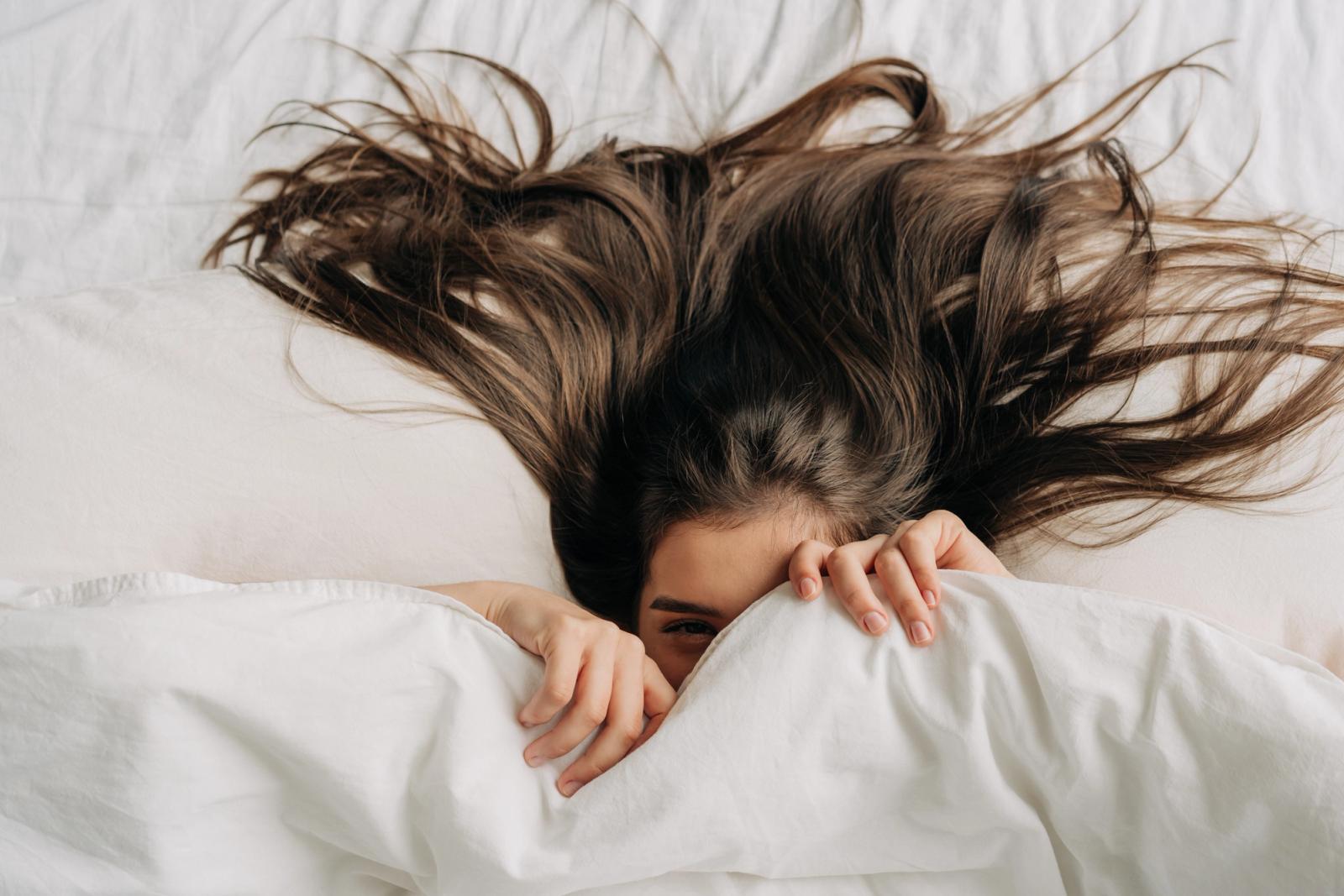 Woman with long healthy hair covered in sheet lying in bed
