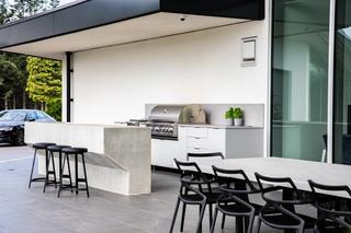Modern outdoor kitchen with white laminate cabinets, a stainless steal grill and black accents. Learn more about outdoor kitchens by Outerpsaces, a Green Theory brand.