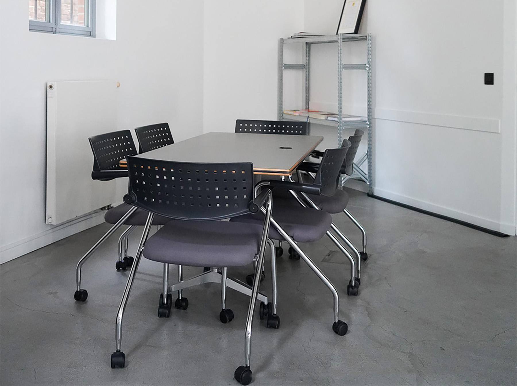 A meeting room furnished with reused task chairs, a meeting table and metal shelving