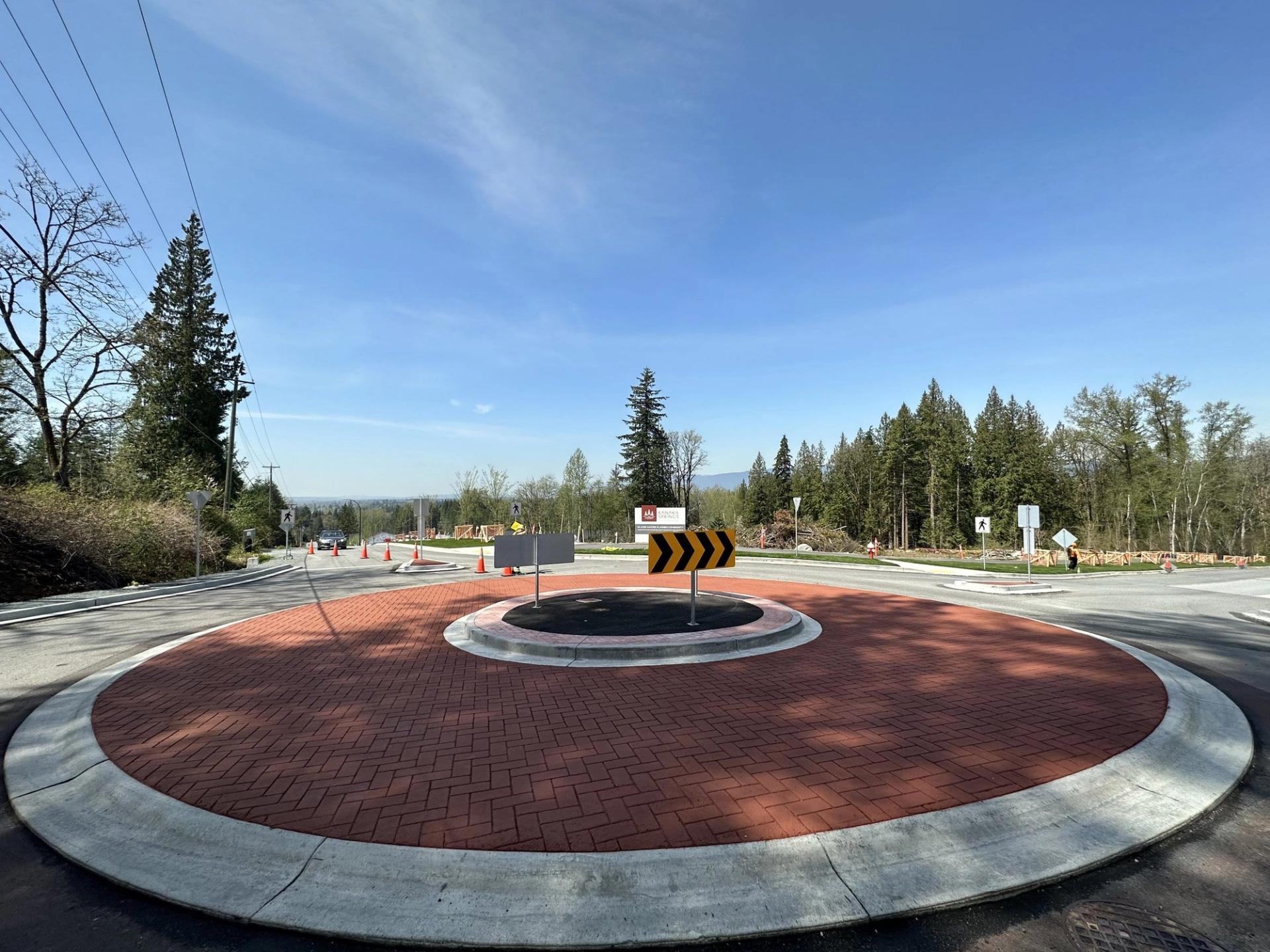 Roundabout with a red brick-pattern stamped apron and chevron signs, forest behind, Maple Ridge, British Columbia