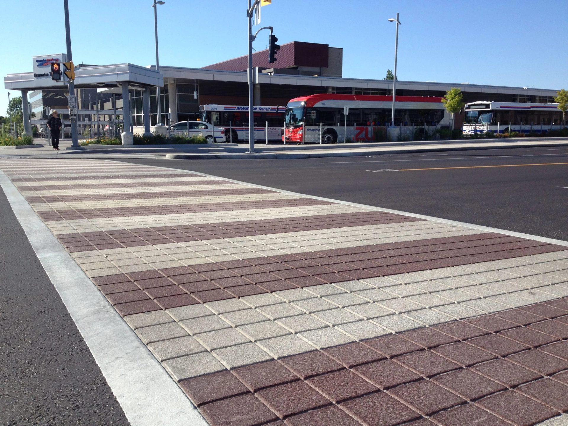 TrafficPatternsXD crosswalk in alternating red and pale brick-pattern bands at a bus terminal, buses at the platforms behind