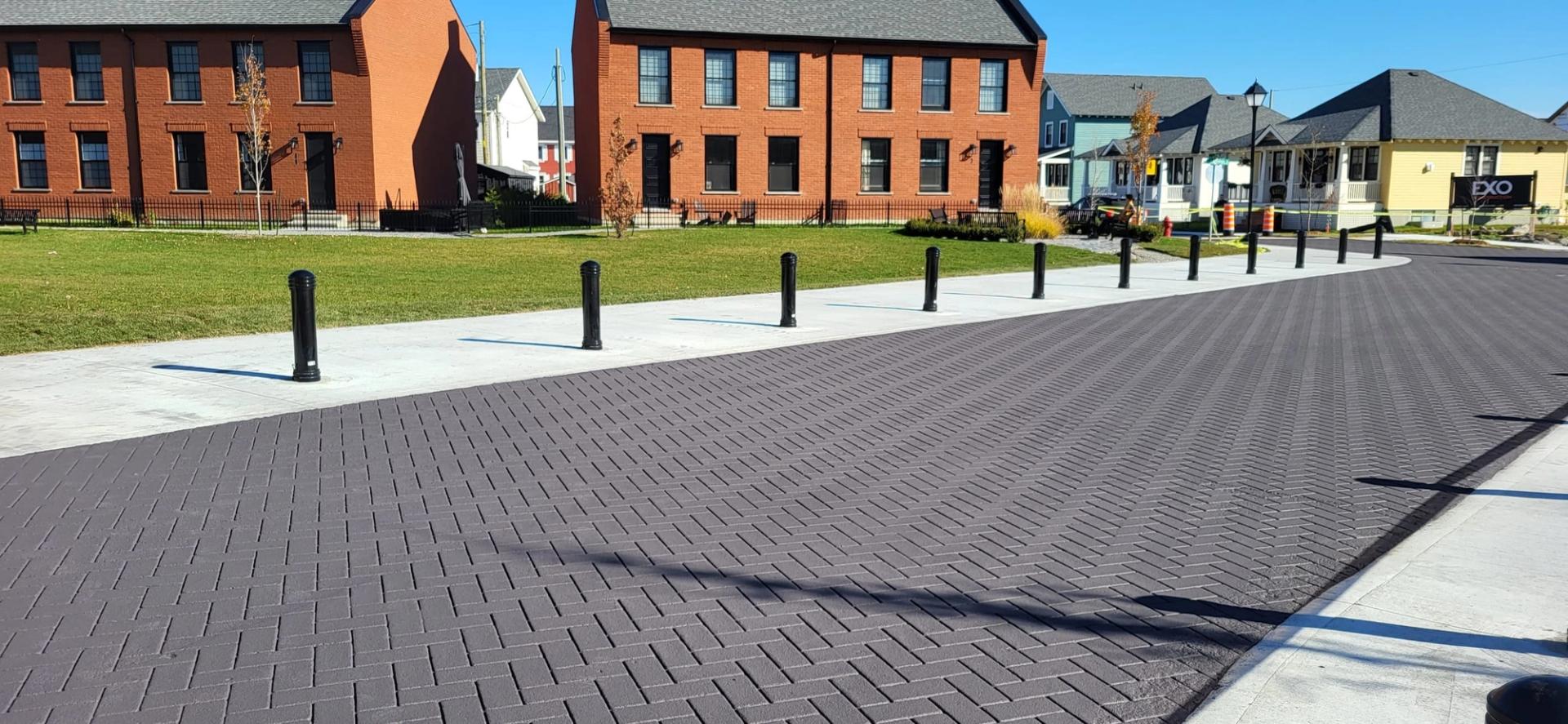 Grey StreetPrint herringbone roadway lined with black bollards in front of new brick townhomes