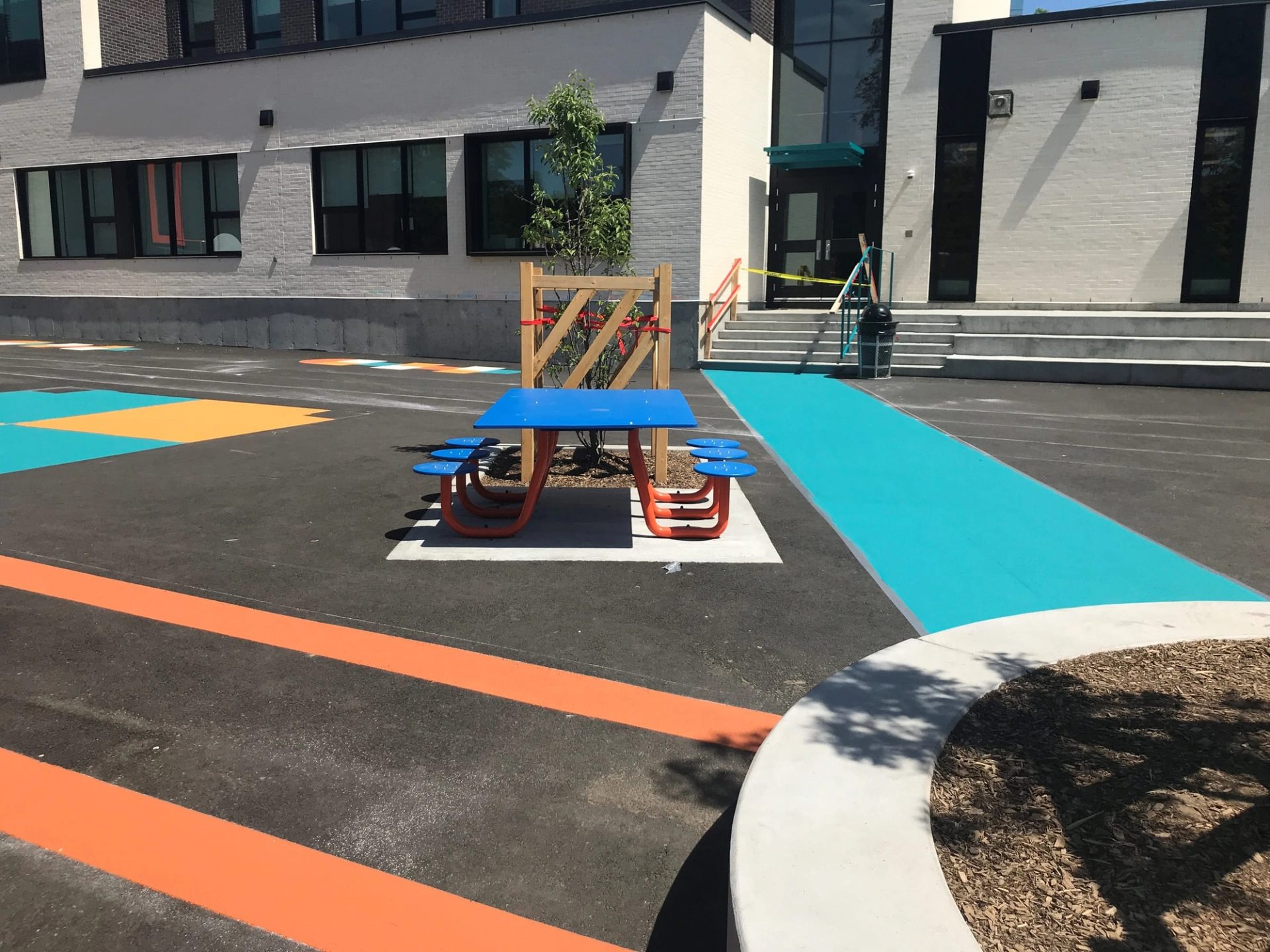 Schoolyard coated with turquoise, orange and yellow play markings around a blue picnic table
