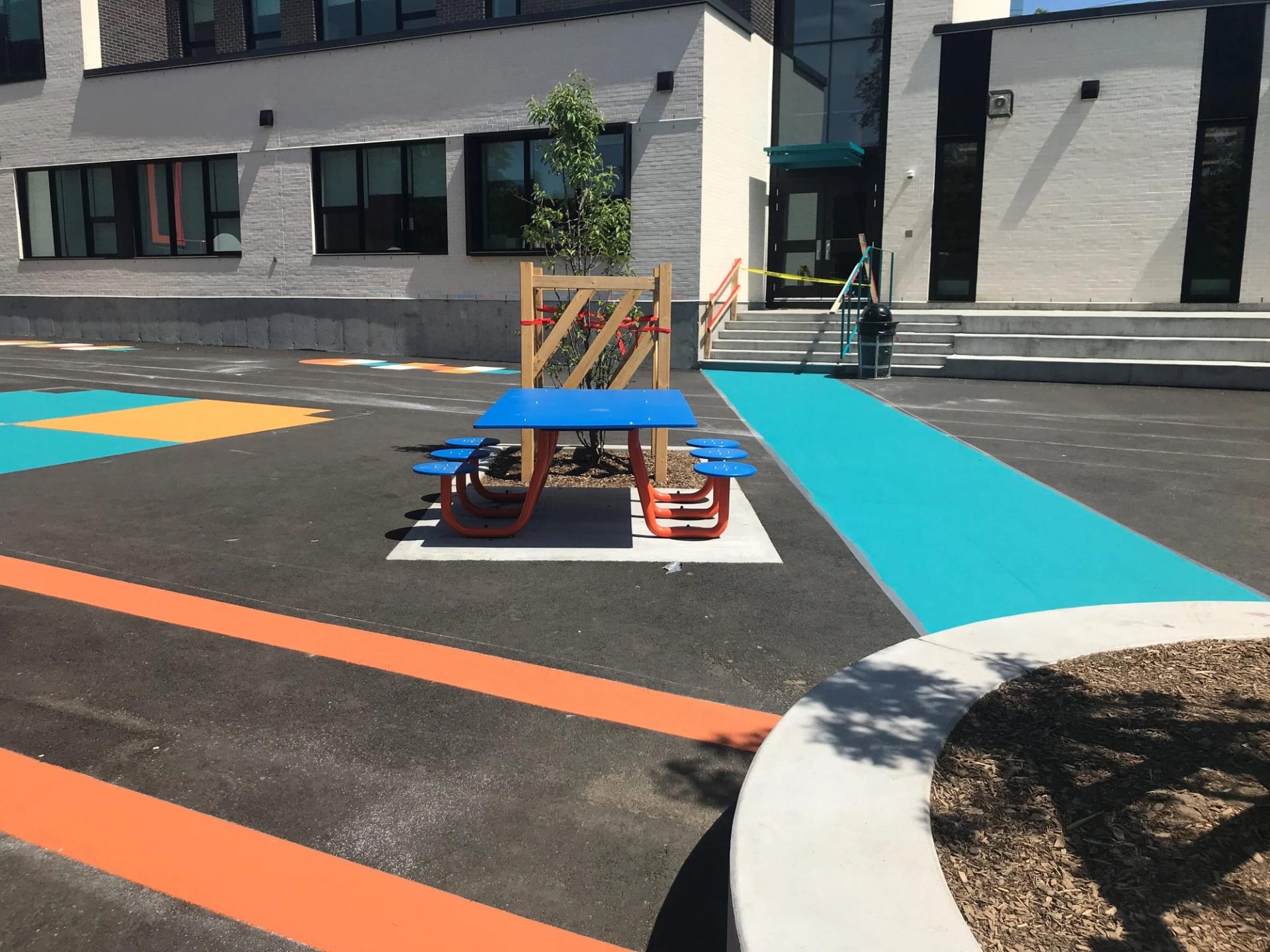 Schoolyard coated with turquoise, orange and yellow play markings around a blue picnic table