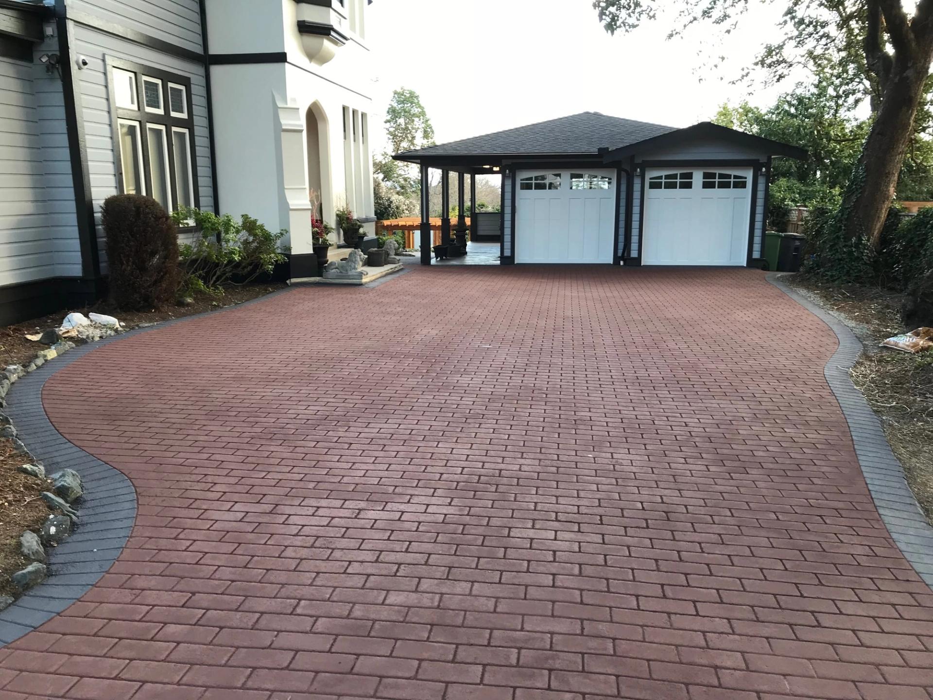 Red brick-pattern stamped asphalt driveway curving to a double garage beside a white house