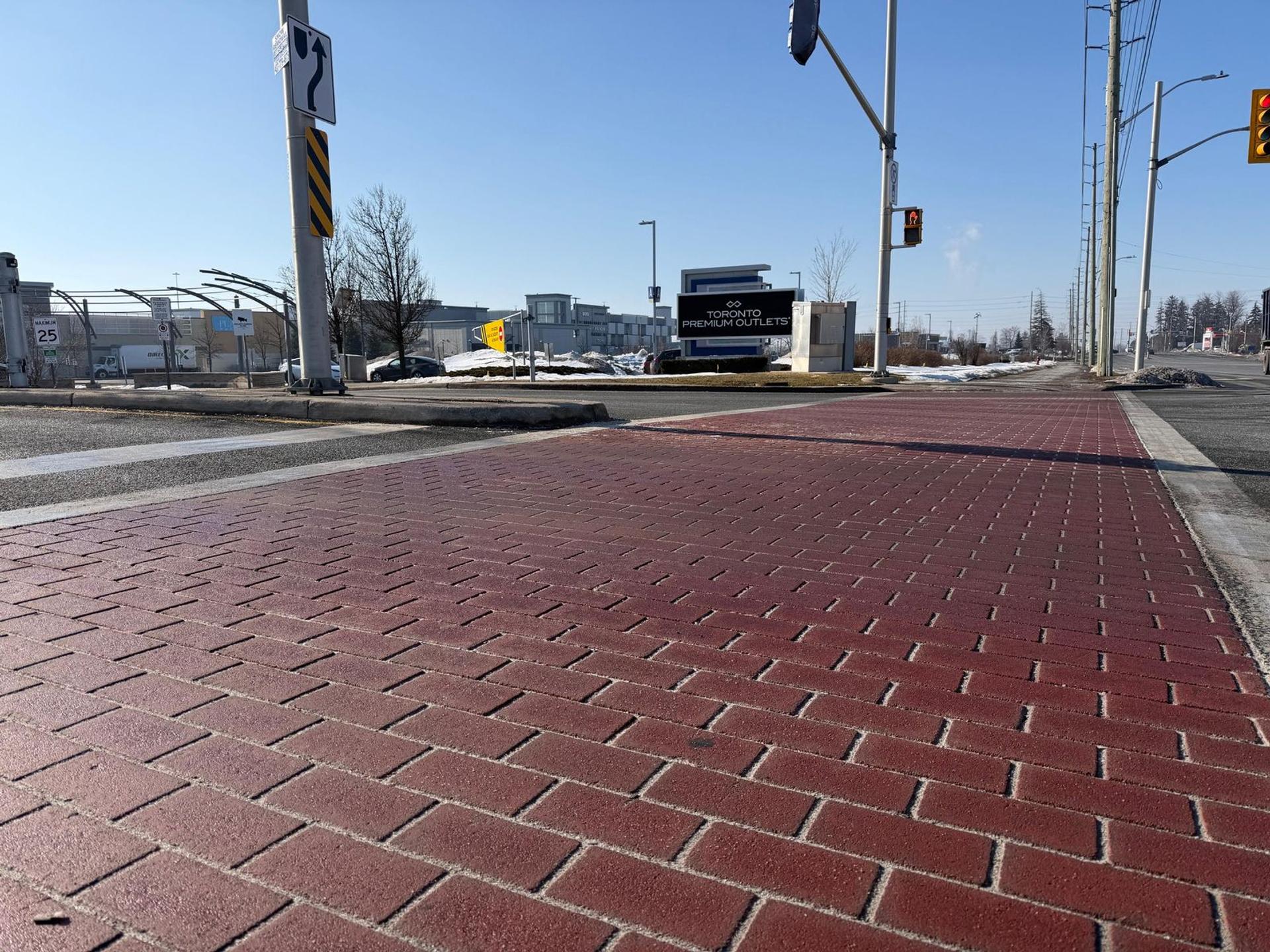 The brick-pattern TrafficPatternsXD crosswalk at the entrance to Toronto Premium Outlets in Halton Hills, Ontario, fourteen years in service, with the outlets' sign behind