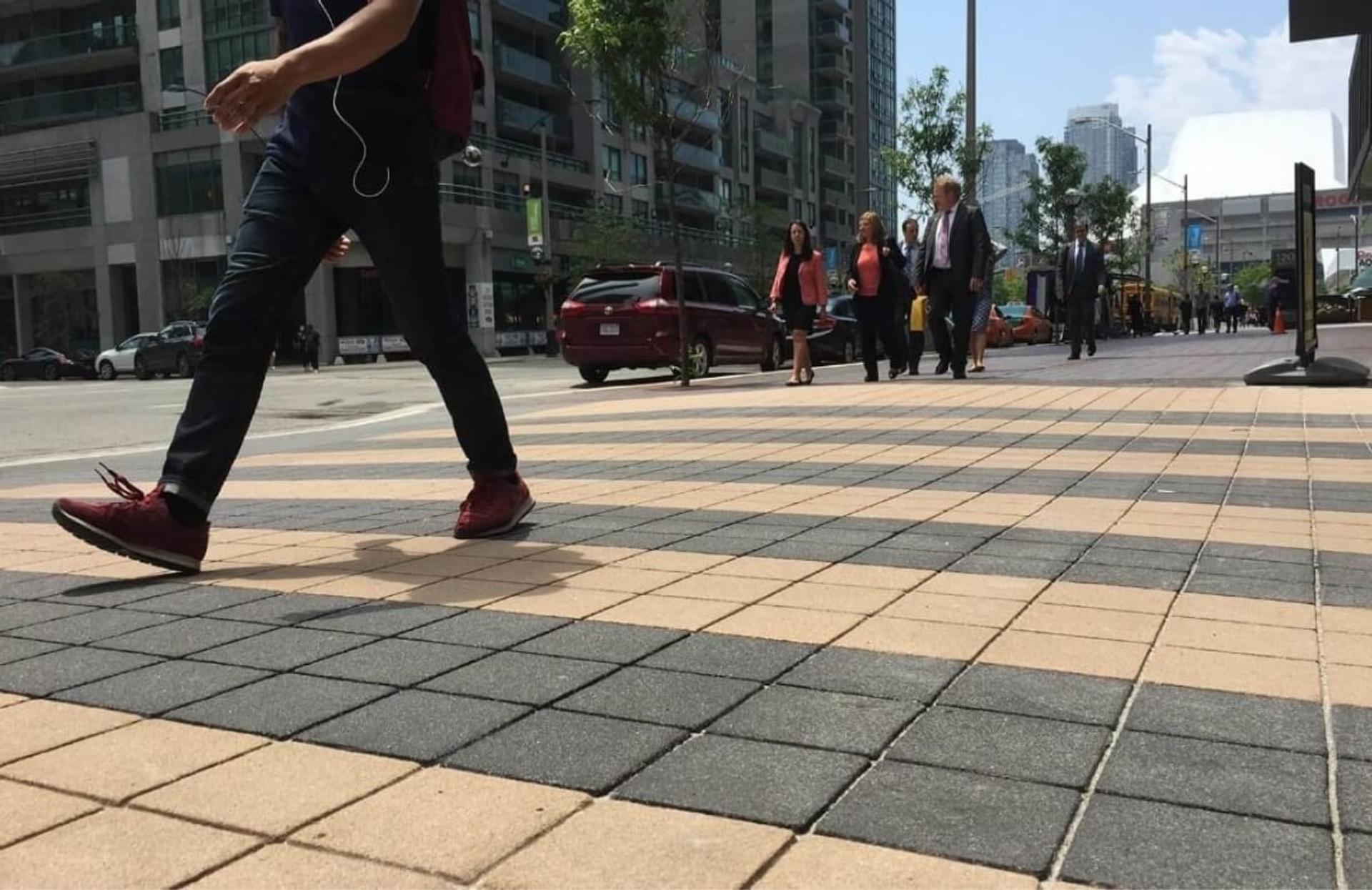 A pedestrian walking across a TrafficPatternsXD crosswalk of tan and charcoal squares in downtown Toronto, Ontario