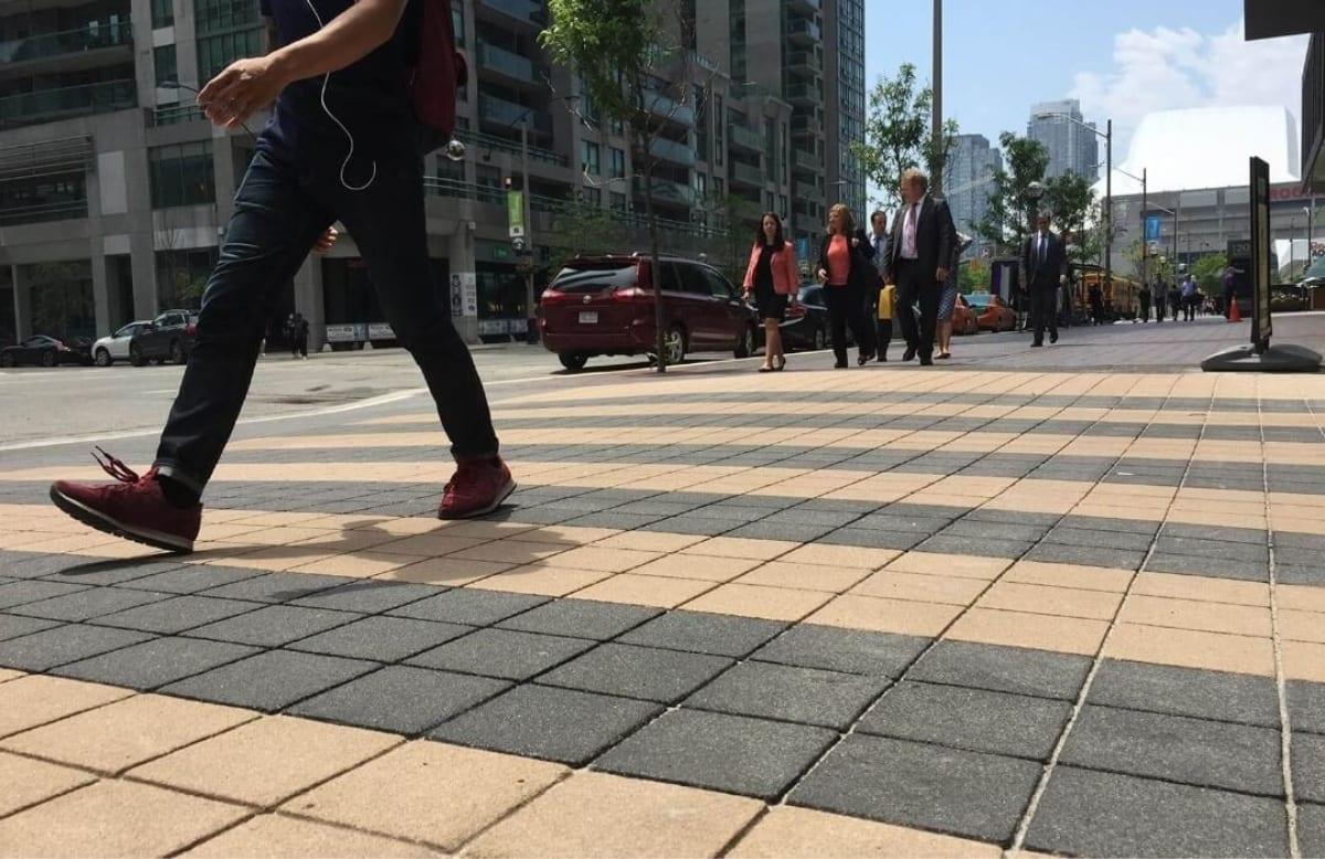 A pedestrian walking across a TrafficPatternsXD crosswalk of tan and charcoal squares in downtown Toronto, Ontario