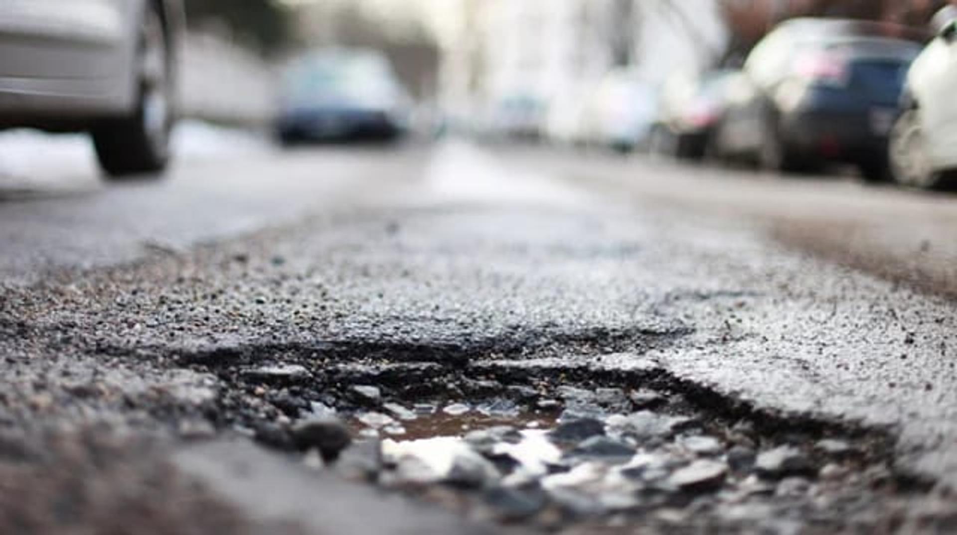 A pothole in an asphalt street, parked cars blurred behind: the damage ChipFill repairs