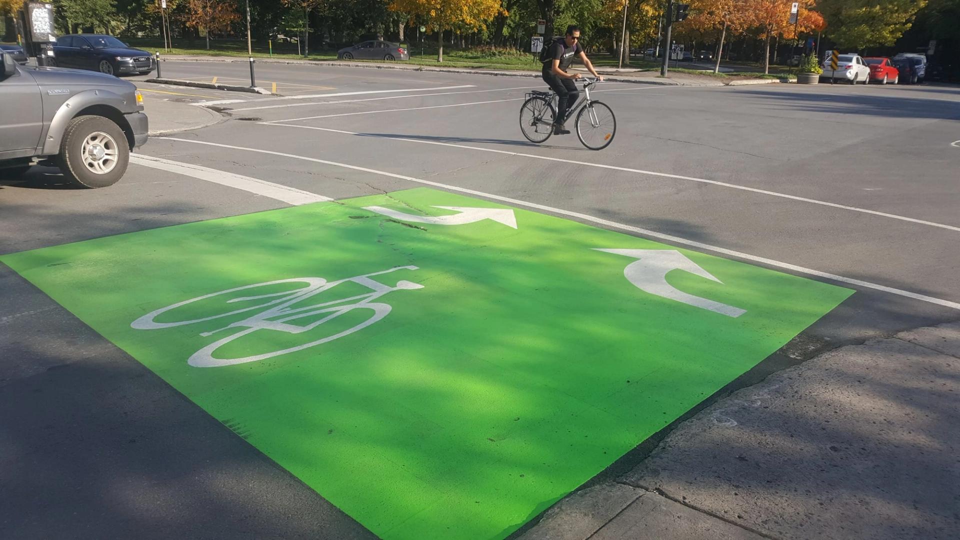 Green bike box with a white bicycle symbol and turn arrows at an intersection, a cyclist riding past