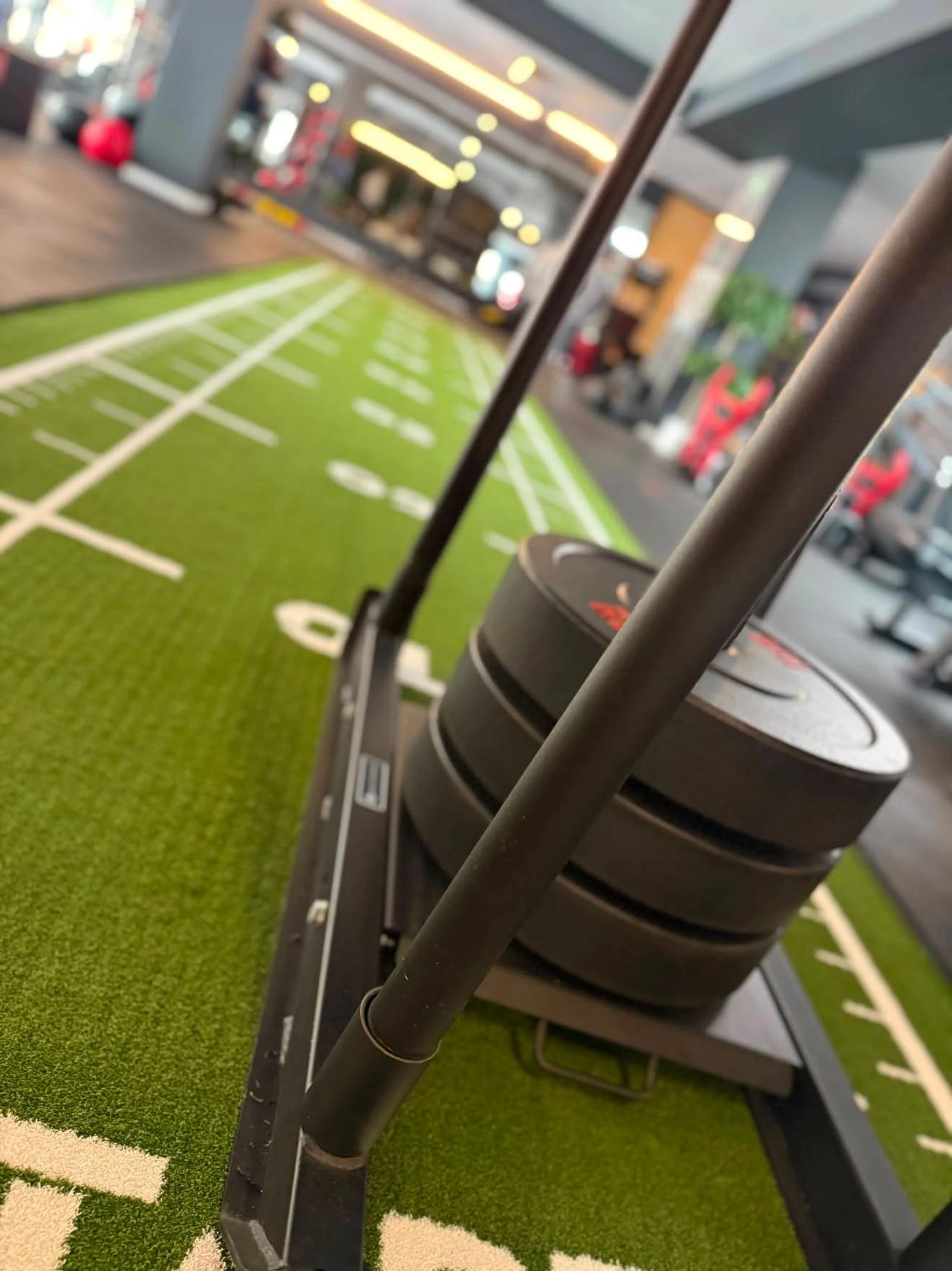 Sled loaded with four weight plates on the green Elysium track, white lane markings running ahead into the gym