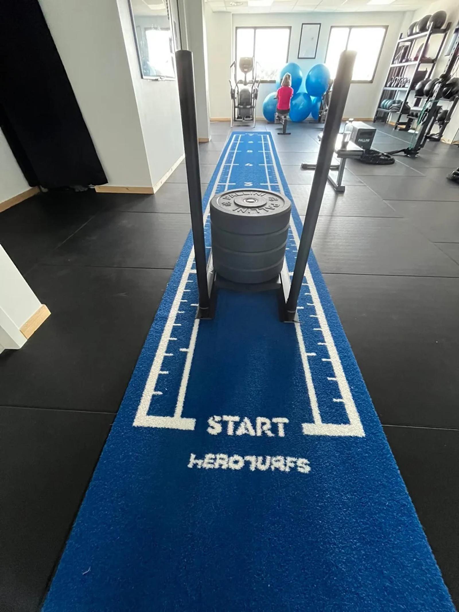 Loaded sled sitting at the START of the 8 m blue turf track at Centre Santé & Performance