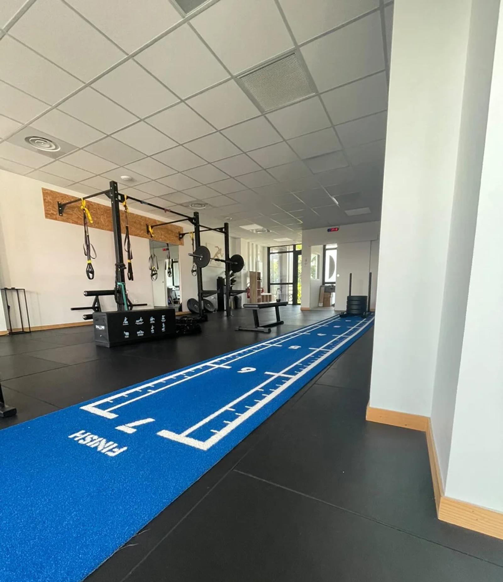 The blue turf lane crossing the training room towards the cardio machines at Centre Santé & Performance