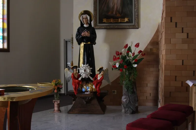 Relikwiarz z figurą Faustyny w ciemnym habicie oraz małymi aniołami przy podstawie, we wnętrzu kościoła.