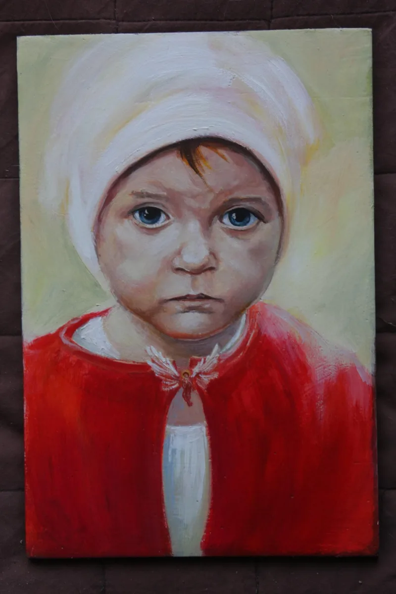 Portret dziecka w jasnej czapce i czerwonym ubraniu.