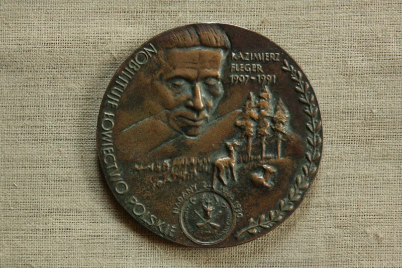 Okrągły medal z portretem Kazimierza Flegera, napisami i drobnymi elementami krajobrazu.