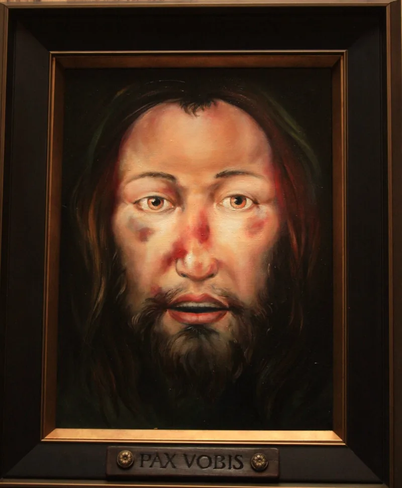 Portret brodatego mężczyzny z długimi włosami, w ramie z napisem „Pax vobis”.