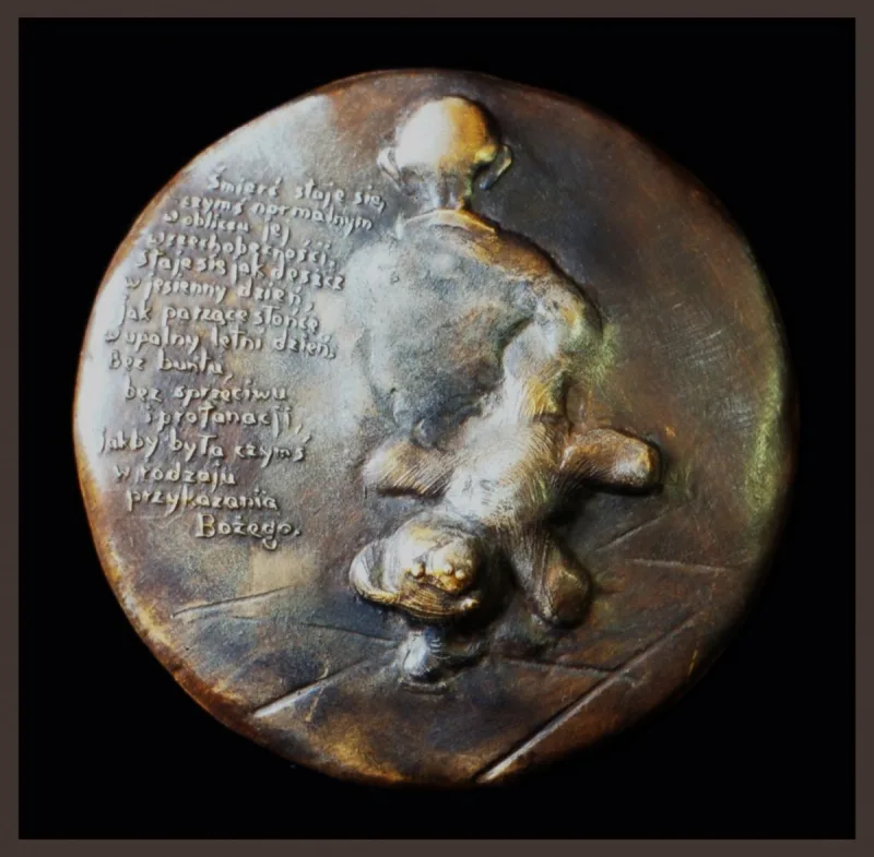 Okrągły medal z napisem oraz nieregularną wypukłą formą na prawej połowie.