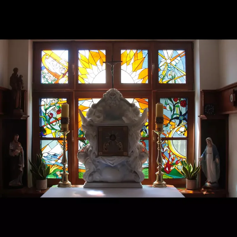 Tabernakulum na tle barwnych okien, ujęte wraz z otaczającym wyposażeniem wnętrza.