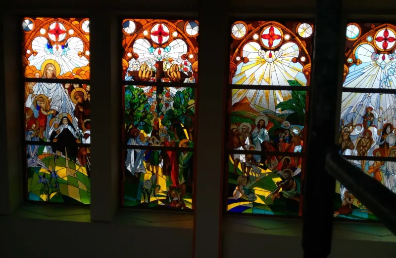 Zestaw sąsiadujących witraży z wielobarwnymi scenami figuralnymi w ciemnym wnętrzu.