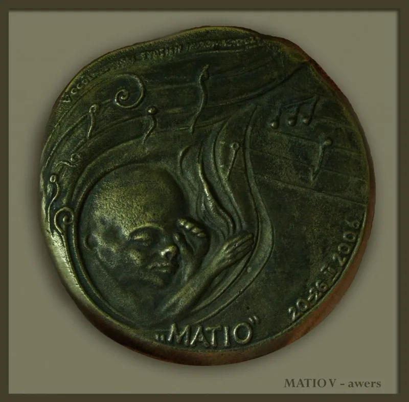 Okrągły medal z twarzą dziecka w zawijających się formach i napisem MATIO.