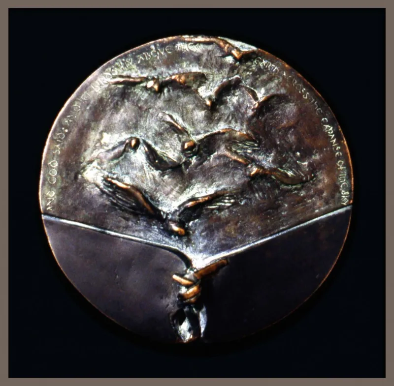 Okrągły medal z wypukłymi sylwetkami ptaków i wyraźnym podziałem powierzchni.