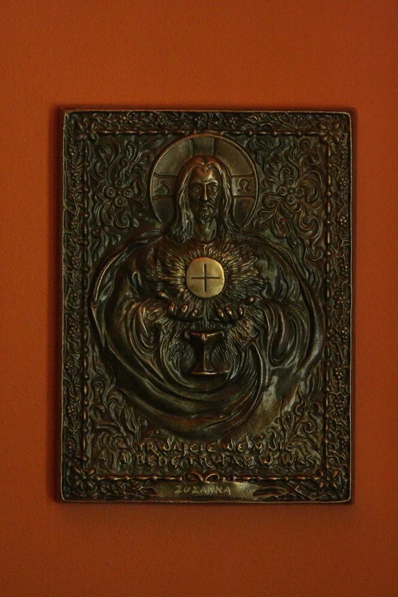Prostokątna płaskorzeźba Jezusa trzymającego okrągły element, otoczona gęstym ornamentem.