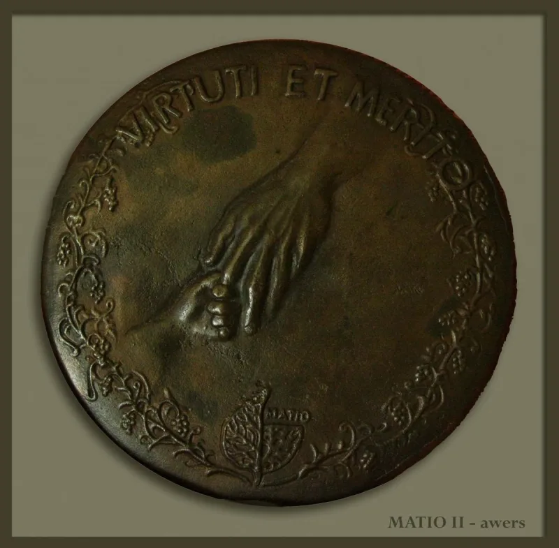 Okrągły medal z dłońmi, drobnym przedmiotem i napisem „Virtuti et merito”.