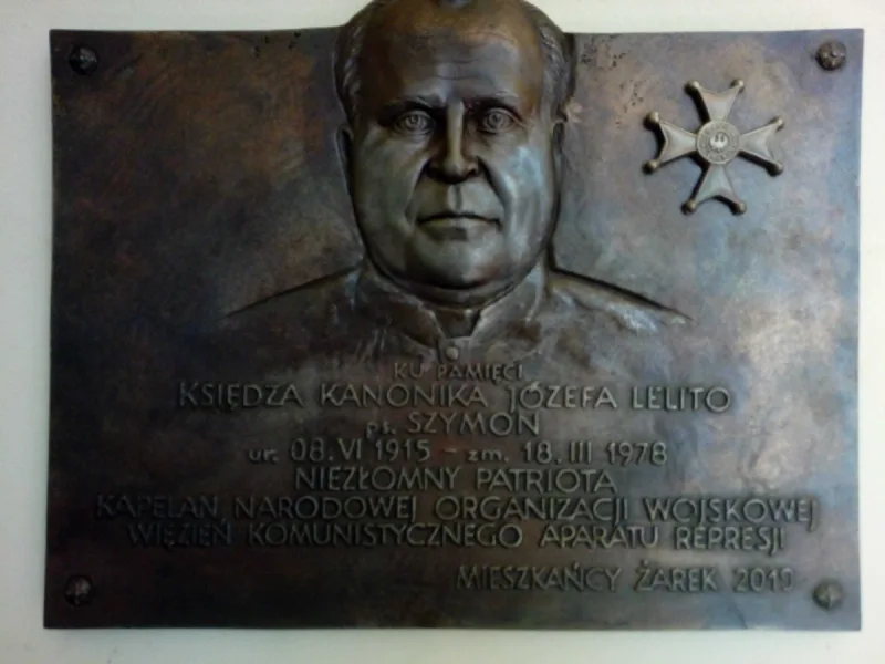 Prostokątna tablica z portretem księdza Józefa Lelity, krzyżem i napisem poniżej.