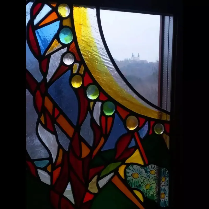 Detal witraża z jasnym kolistym polem oraz czerwonymi, niebieskimi i zielonymi fragmentami szkła.