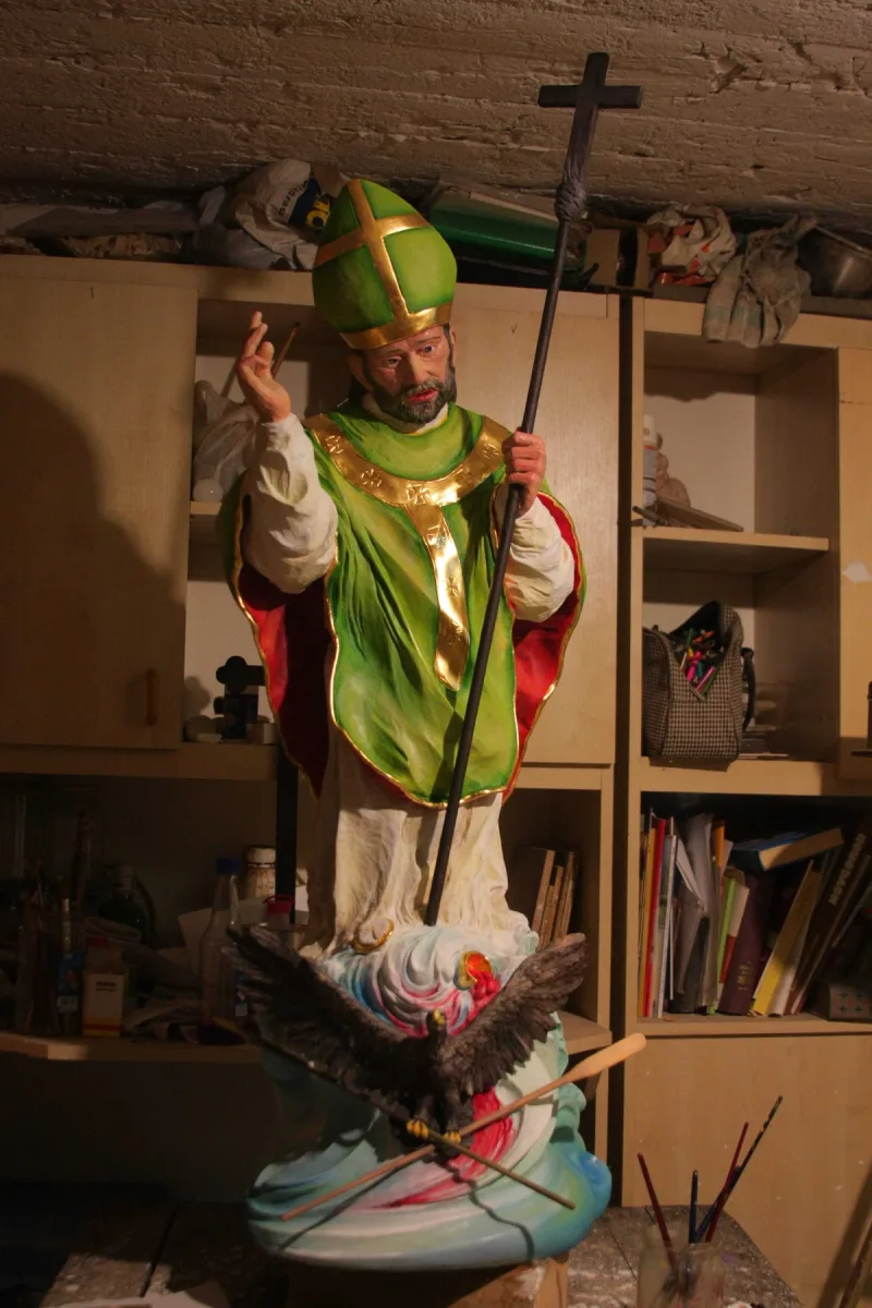Figura św. Wojciecha w zielonych szatach i mitrze, trzymającego wysoki krzyż.