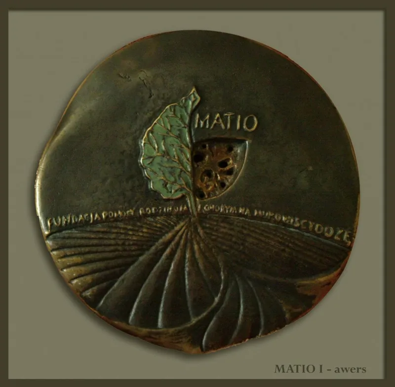 Okrągły medal z liściem, napisem MATIO i promieniście rozchodzącymi się liniami.