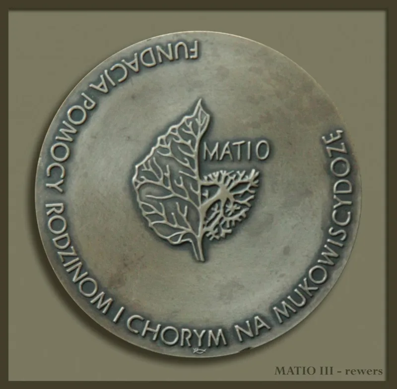 Okrągły medal z motywem liści, napisem MATIO i napisem biegnącym wzdłuż obwodu.