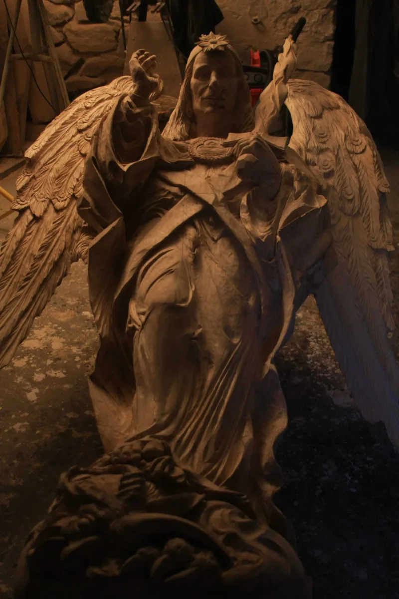 Figura anioła z rozpostartymi skrzydłami i uniesioną dłonią, sfotografowana w pracowni.