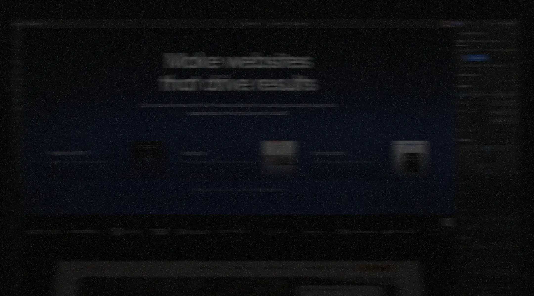 Blurry laptop screen in a dark room displaying a blue website design interface with unreadable text