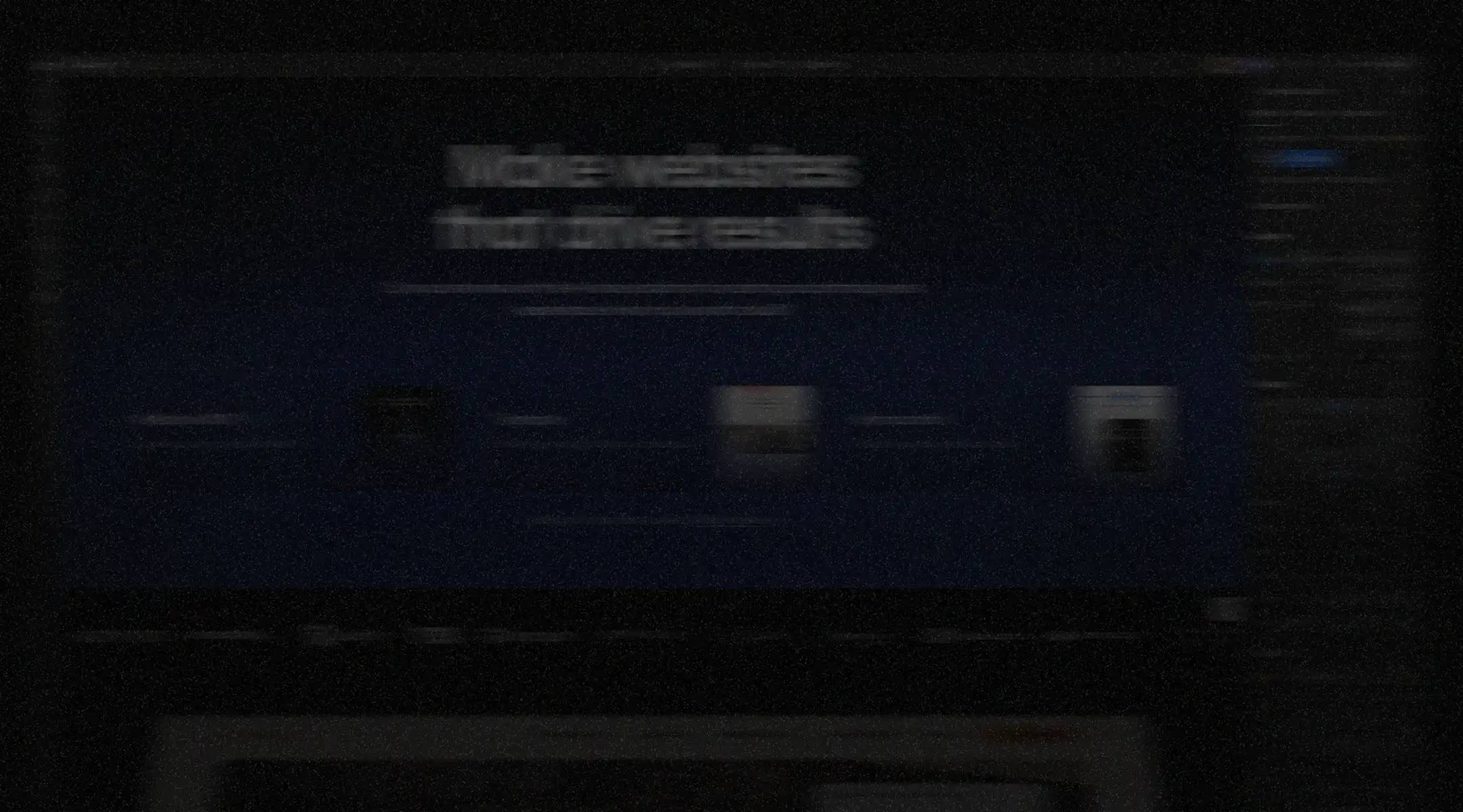 Blurry laptop screen in a dark room displaying a blue website design interface with unreadable text