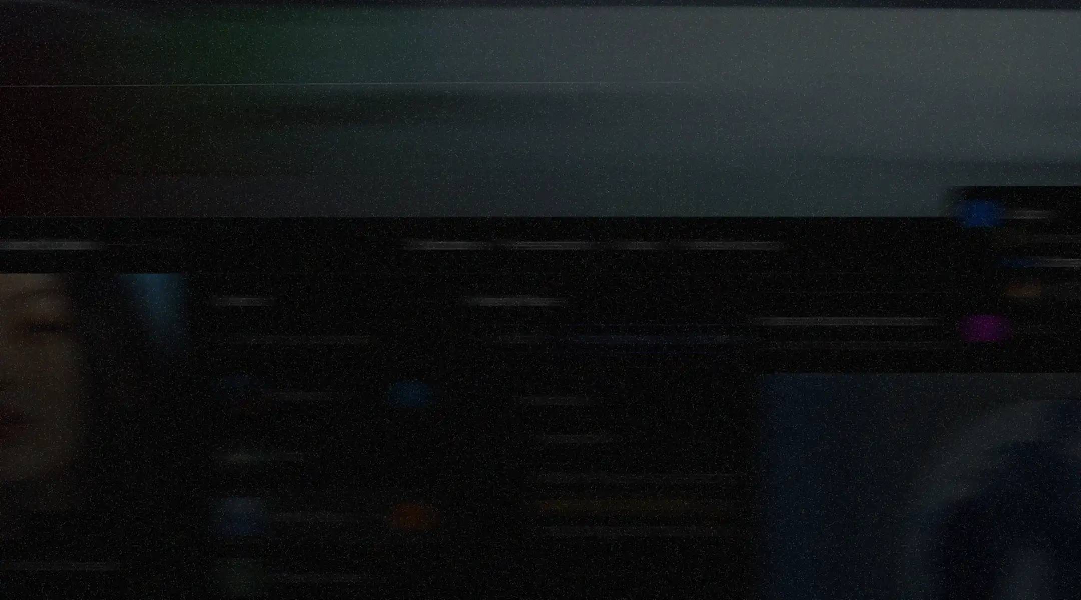Dark, blurred computer screen with faint interface elements and an indistinct face partially visible on the left side.