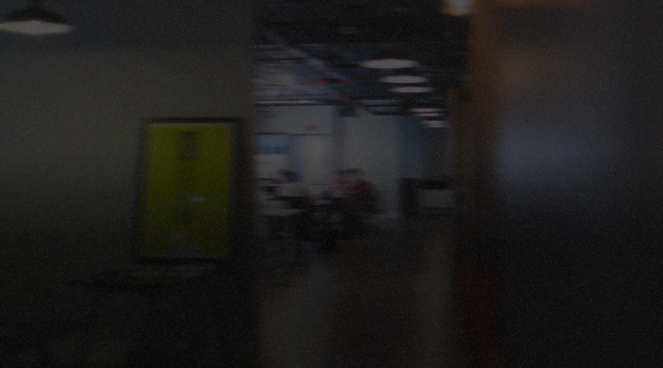 Dimly lit office hallway with a yellow door and people working at desks in the background.