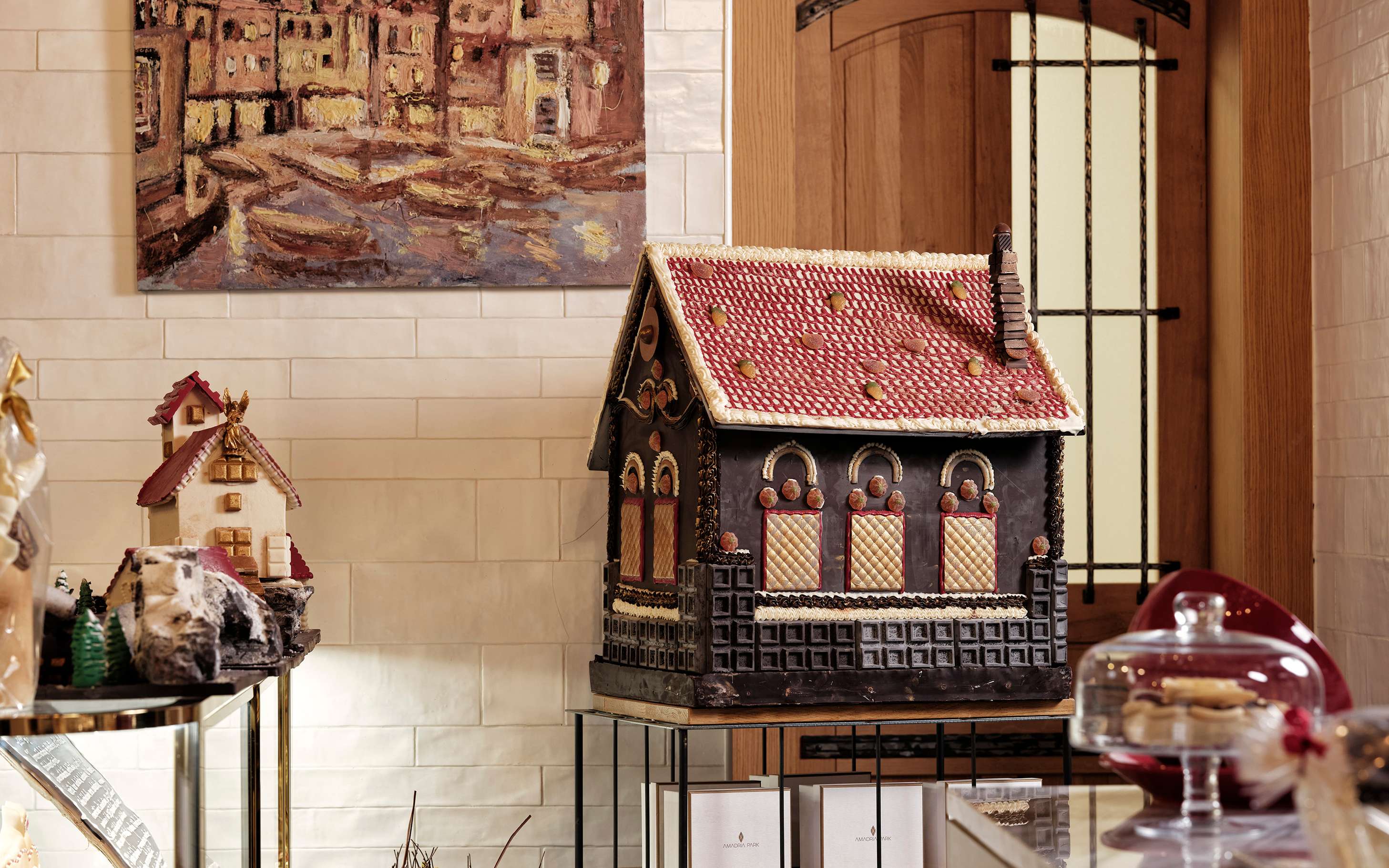 Milenij Choco World: velika čokoladna kuća s crvenim krovom na postolju, uz kolače pod staklenim zvonom.